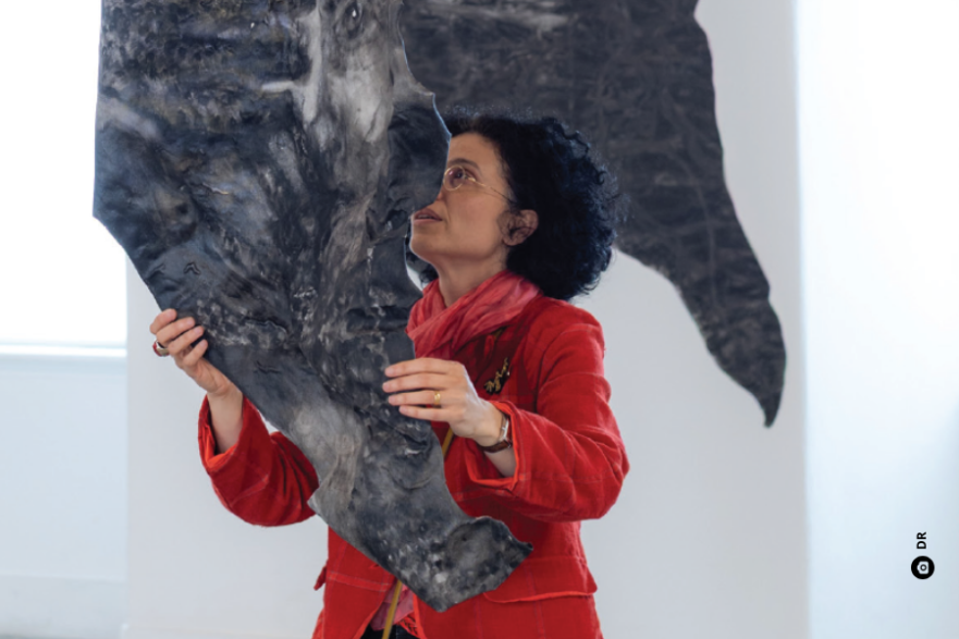 Uma mulher de cabelo escuro e de casaco vermelho segura uma peça de escultura.